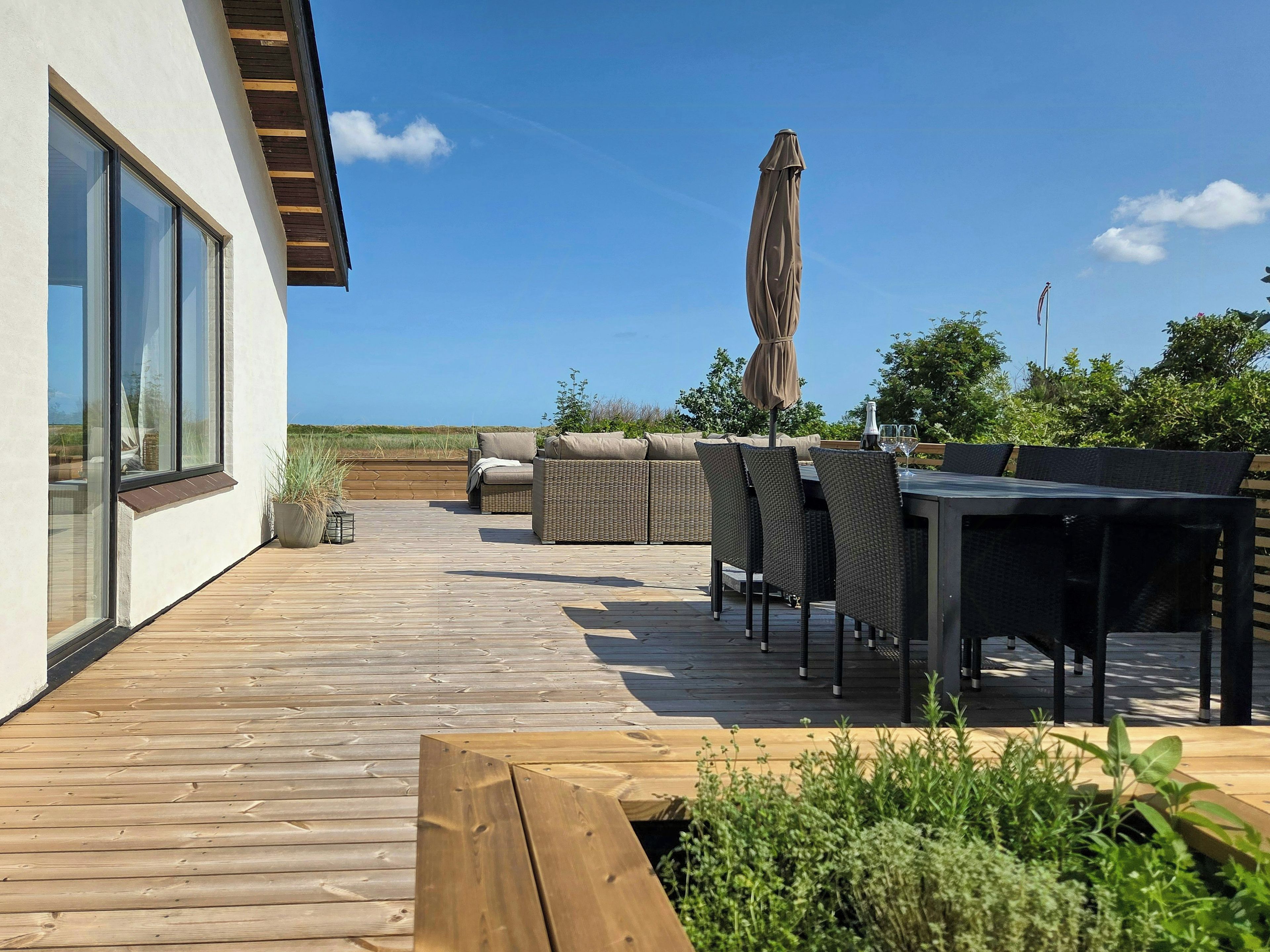 A wooden deck with outdoor furniture, including a table and chairs, and a large umbrella.