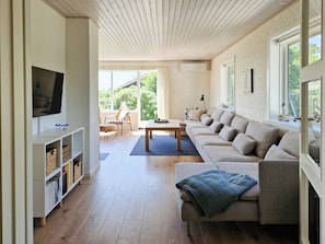 A modern living room with a sofa, TV, bookshelf, and a view of greenery outside. - Beach house with sea view near Hou beach (Hals)