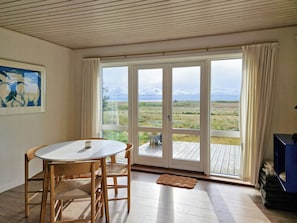 A room with a dining table and chairs, a large sliding glass door leading to an outdoor deck, and a painting on the wall. - Beach house with sea view near Hou beach (Hals)