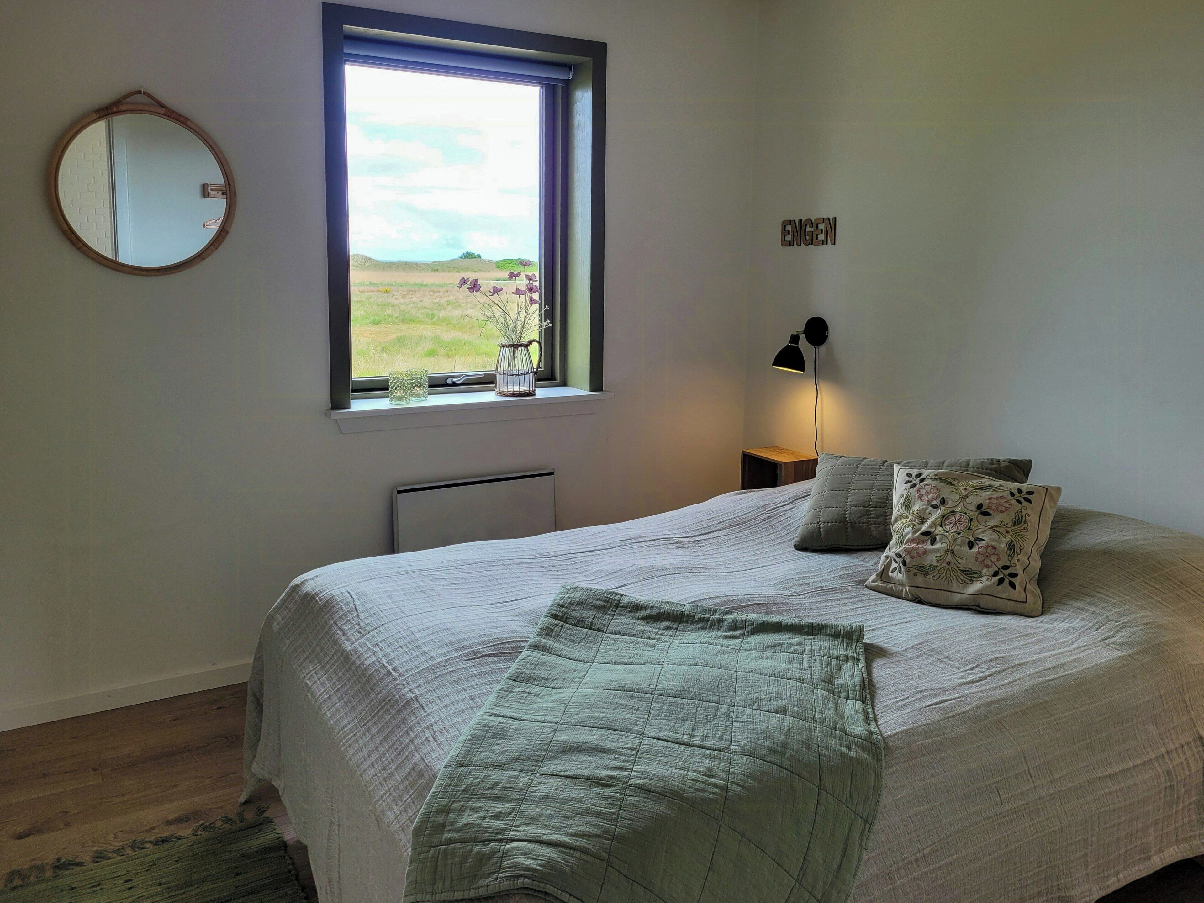 Une chambre à coucher avec un lit, une fenêtre, une lampe fixée au mur et un miroir.