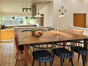 A wooden dining table with chairs, a kitchen area with wooden cabinets, and a window with a view of the outside. - Beach house with sea view near Hou beach (Hals)