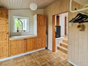 A kitchen with wooden cabinets, a window with a view, a refrigerator, and a hanging rack. - Beach house with sea view near Hou beach (Hals)