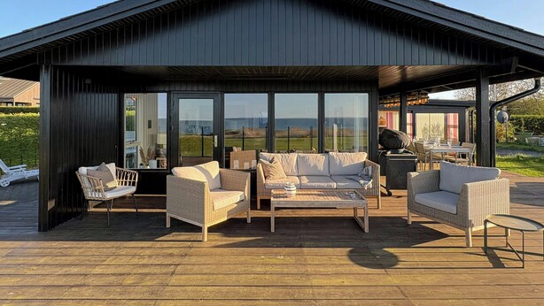 A covered outdoor seating area with wicker furniture and a view of the landscape. - Summer house with sea view on Fyn (Asperup)
