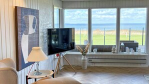 A modern living room with a large TV, comfortable seating, a lamp, and a view of the sea. - Summer house with sea view on Fyn (Asperup)