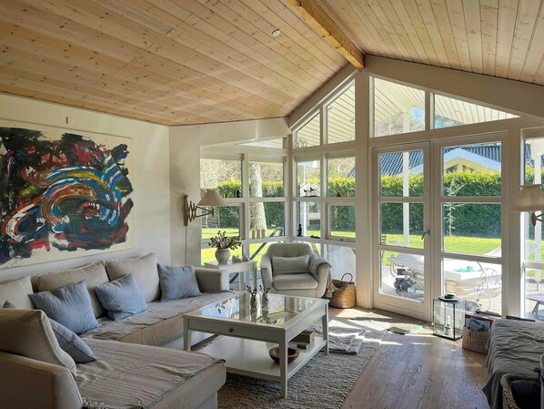 A spacious living room with a large window, a modern sofa, a glass coffee table, and a large abstract painting on the wall. - Holiday home with sauna near Anneberg (Højby)