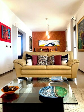 Ein Wohnzimmer mit einem beigen Sofa, einem Glastisch und einem Gemälde an der Wand.