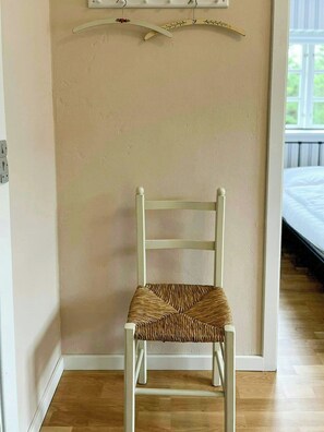 A white woven chair in a room with a wooden floor, beige walls, and a window with a view of a balcony. - Retro holiday home by Thy National Park (Bedsted)