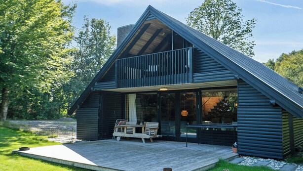 A modern log cabin with a balcony, a deck, and a dining area. - 70s holiday home with fjord views at Lyby Beach (Roslev)