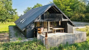 A wooden cabin with a balcony, a deck, and a dining area. - 70s holiday home with fjord views at Lyby Beach (Roslev)