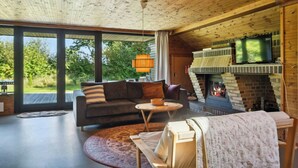 A cozy living room with a fireplace, a sofa, a coffee table, and a TV. - 70s holiday home with fjord views at Lyby Beach (Roslev)
