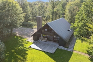 Eine Hütte mit Terrasse, Schornstein und bewaldeter Landschaft im Hintergrund.