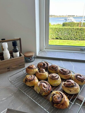 Un piano di lavoro della cucina con cinnamon rolls raffreddati su una griglia, un saliera e una pepe in una scatola di legno.