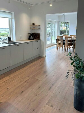 Una cucina moderna con pavimento in legno, un'area pranzo con sedie di legno e un'ampia finestra che offre una vista.