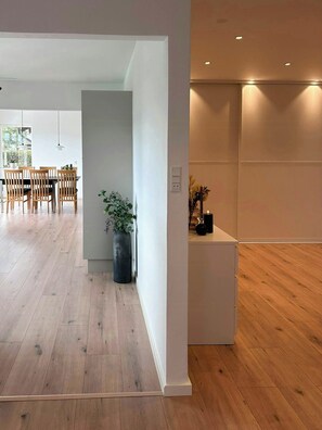 Un interno moderno con pavimento in legno, zona pranzo con sedie, una pianta in vaso e illuminazione a incasso.