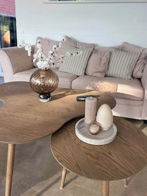 Un soggiorno moderno con un tavolino rotondo in legno, un divano beige con cuscini a righe e un vaso con fiori bianchi.