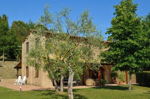 A rustic stone building with a patio area, outdoor seating, and a large tree in the foreground. - Private pool stone villa overlooking Crete Senesi (Asciano)