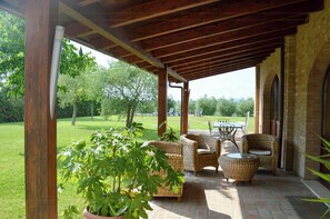 A covered patio with wicker furniture, a potted plant, and a view of a grassy area. - Private pool stone villa overlooking Crete Senesi (Asciano)