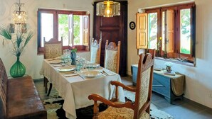 Een eetkamer met een tafel voor vier personen, houten stoelen, een kroonluchter en ramen met houten luiken.