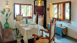 A dining room with a table set for four, wooden chairs, a chandelier, and windows with wooden shutters. - Villa with 360° panoramic sea views and a jacuzzi (Caccamo)