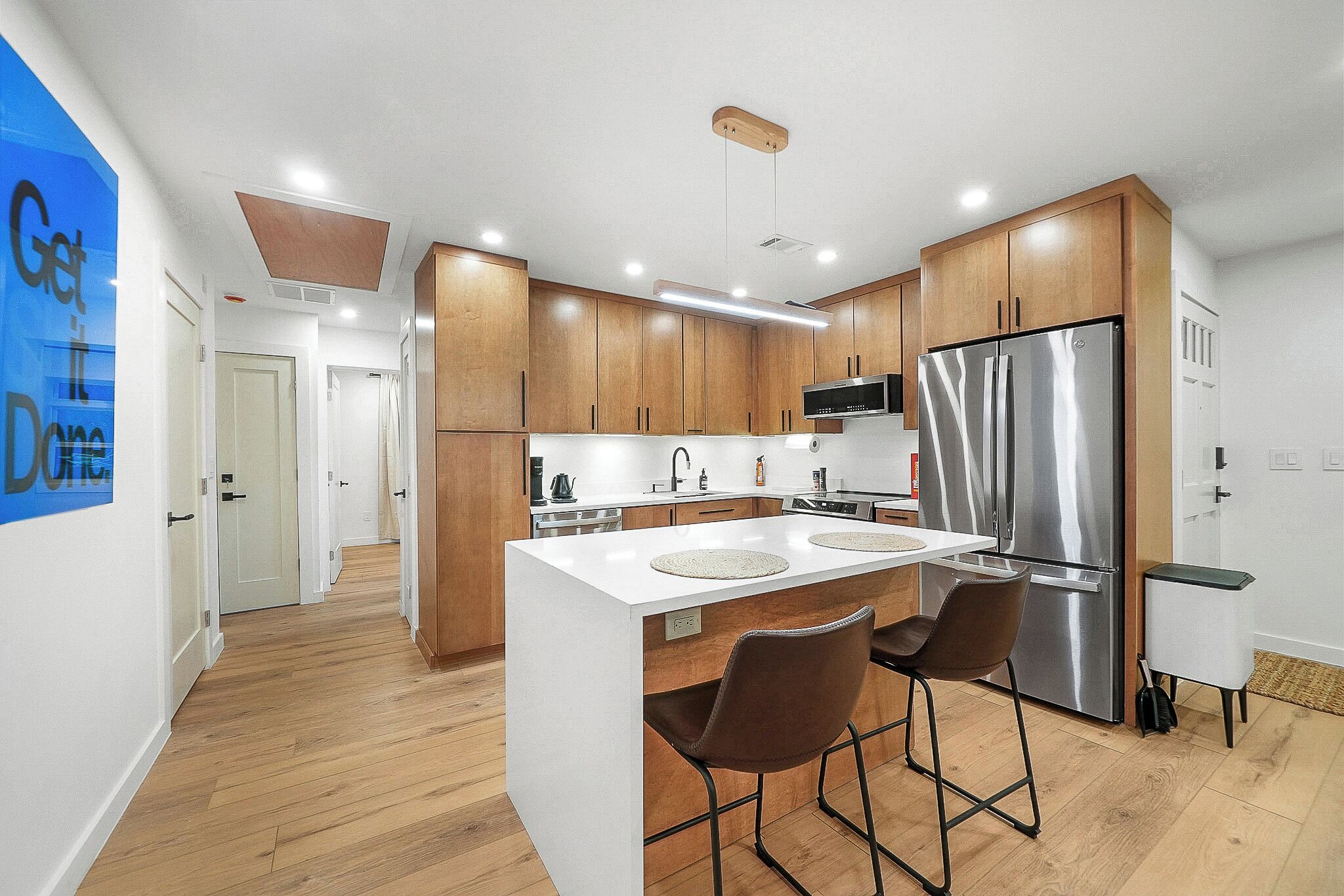 A modern kitchen with wooden cabinets, a stainless steel refrigerator, and a bar area with stools.