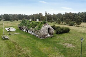 A thatched-roof structure with a grassy roof, surrounded by a well-maintained lawn and trees in the background. - Renovated stable with seaweed roof on Læsø (Læsø)