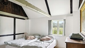 Une chambre avec un lit simple, une commode en bois, une fenêtre donnant sur un beau paysage et des poutres apparentes.