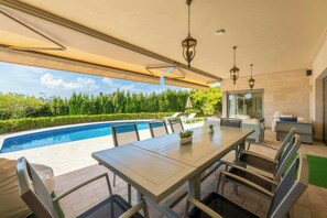 Un espace extérieur abrité, aménagé pour les repas, avec une piscine, des chaises longues et une table avec des chaises.