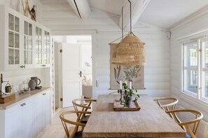 Ein Essbereich mit Holztisch, Korbstühlen, einer Hängelampe und einem weißen Schrank mit Glastüren.