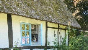 Une maison à toit de chaume avec une fenêtre et une chaise dans le jardin.