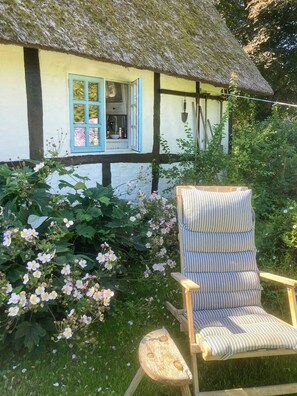 Ein Haus mit einem Strohdach, einem Fenster und einem Stuhl im Garten.