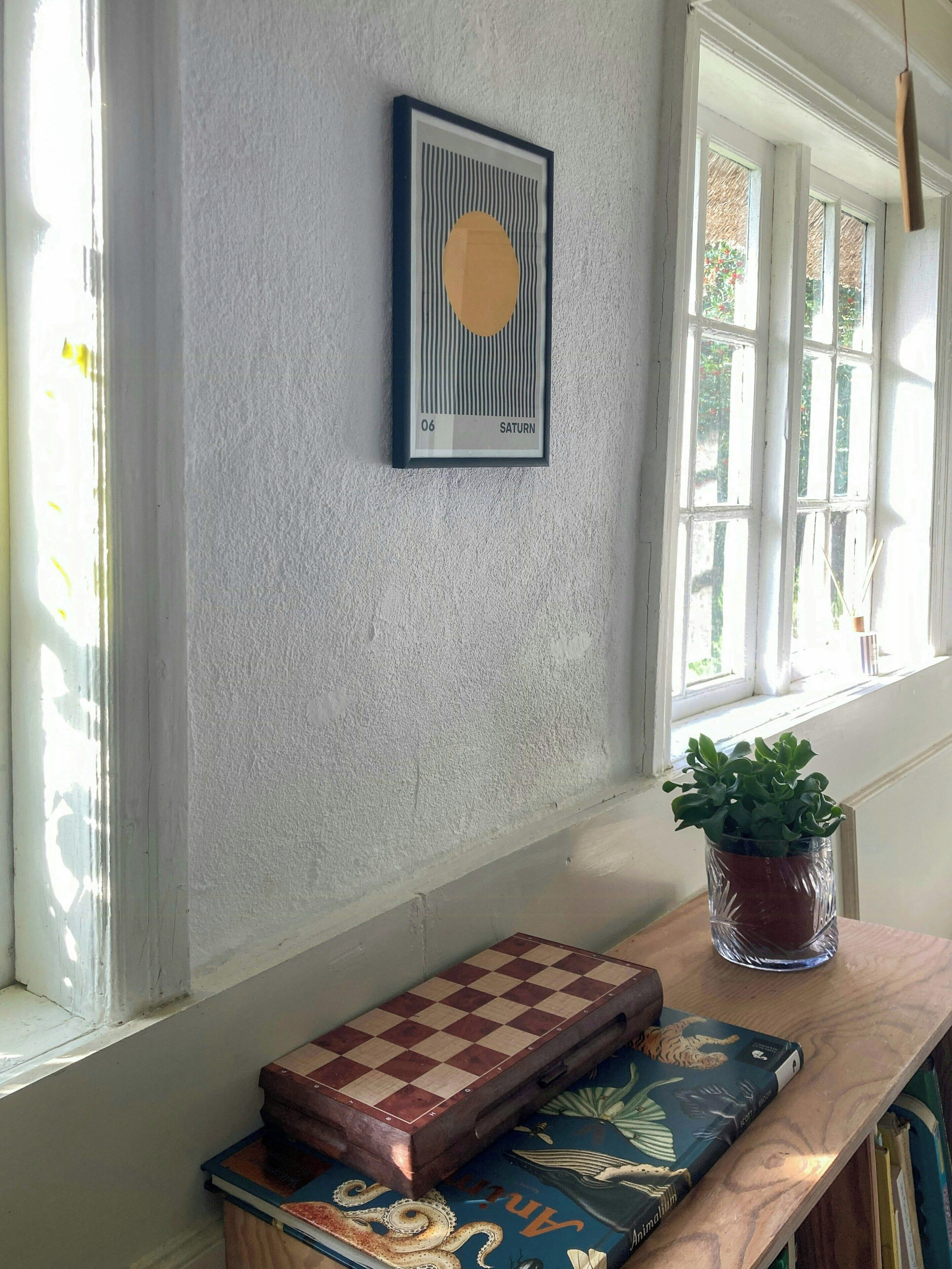 A room with a framed artwork, a chessboard, and a potted plant.