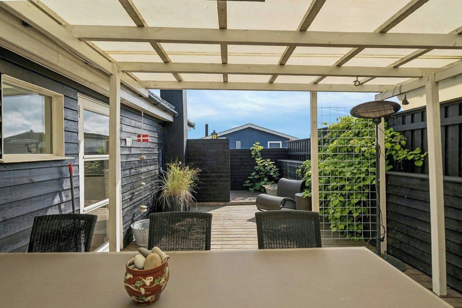 A covered patio with a table and chairs, a potted plant, and a view of a backyard.