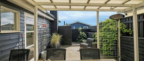 A covered patio with a table and chairs, a potted plant, and a view of a backyard.