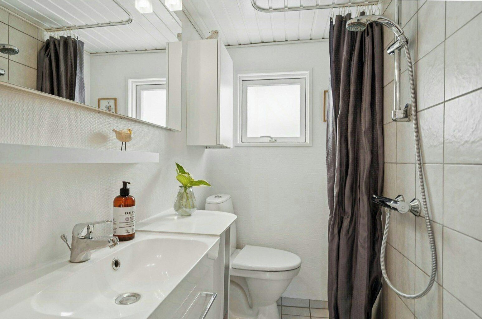 Et badeværelse med vask, toilet, bruser og et lille vindue.