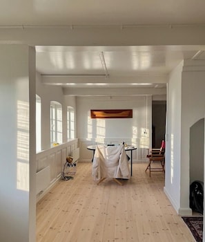Ein geräumiges Zimmer mit großen Fenstern, einem Esstisch und einem Garderobenschrank.