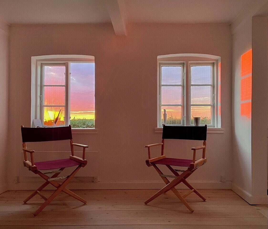 Two director chairs facing two windows with a sunset view.