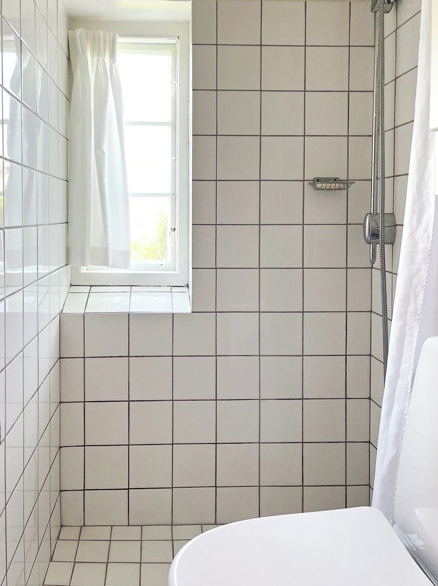 A small, tiled bathroom with a window, a shower, and a toilet.