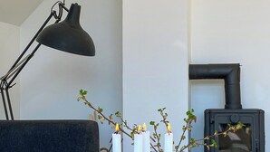 Ein Wohnzimmer mit einer Couch, einem Holztisch, einer schwarzen Stehlampe, einem schwarzen Kaminofen und einer Vase mit Kerzen.