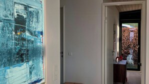 A hallway with a modern abstract painting, a wooden stool, and a view of a garden through a door. - Modern house with sea view near Faaborg (Faaborg)
