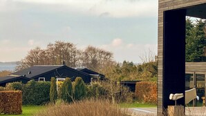 A modern building with a large glass entrance, surrounded by a well-maintained garden with hedges and a hay bale. - Modern house with sea view near Faaborg (Faaborg)