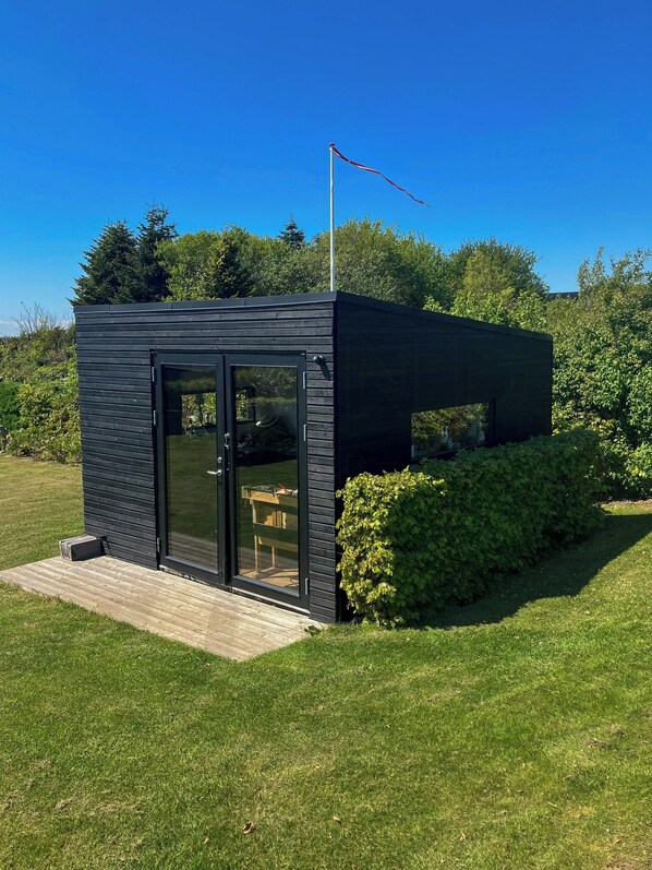 A modern, dark-colored, single-story building with a glass door and windows, surrounded by a well-maintained lawn and greenery.