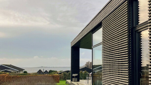 A modern house with a large glass window, a wooden deck, and a view of the sea. - Modern house with sea view near Faaborg (Faaborg)