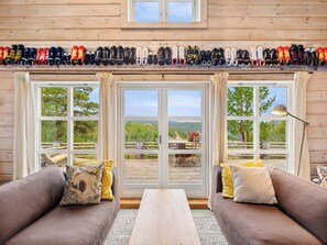 A log cabin interior with a sofa, two windows, a table, and a shoe rack. - Family cabin with hot tub in Hønedalen (Sinnes)