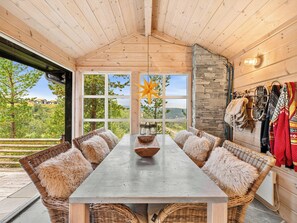 A wooden interior with a large table, wicker chairs, and a stone wall. - Family cabin with hot tub in Hønedalen (Sinnes)