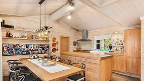 Interior de madera con una isla central, sillas, una composición de fotos en la pared y electrodomésticos de cocina.