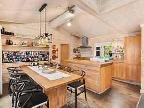 A wooden interior with a central island, chairs, a wall-mounted photo collage, and kitchen appliances. - Family cabin with hot tub in Hønedalen (Sinnes)