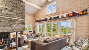 Interior acogedor de una cabaña con una pared de piedra, una chimenea, un sofá seccional y una colección de zapatos en la pared.