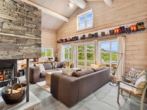 A cozy cabin interior with a stone wall, a fireplace, a sectional sofa, and a collection of shoes on the wall. - Family cabin with hot tub in Hønedalen (Sinnes)