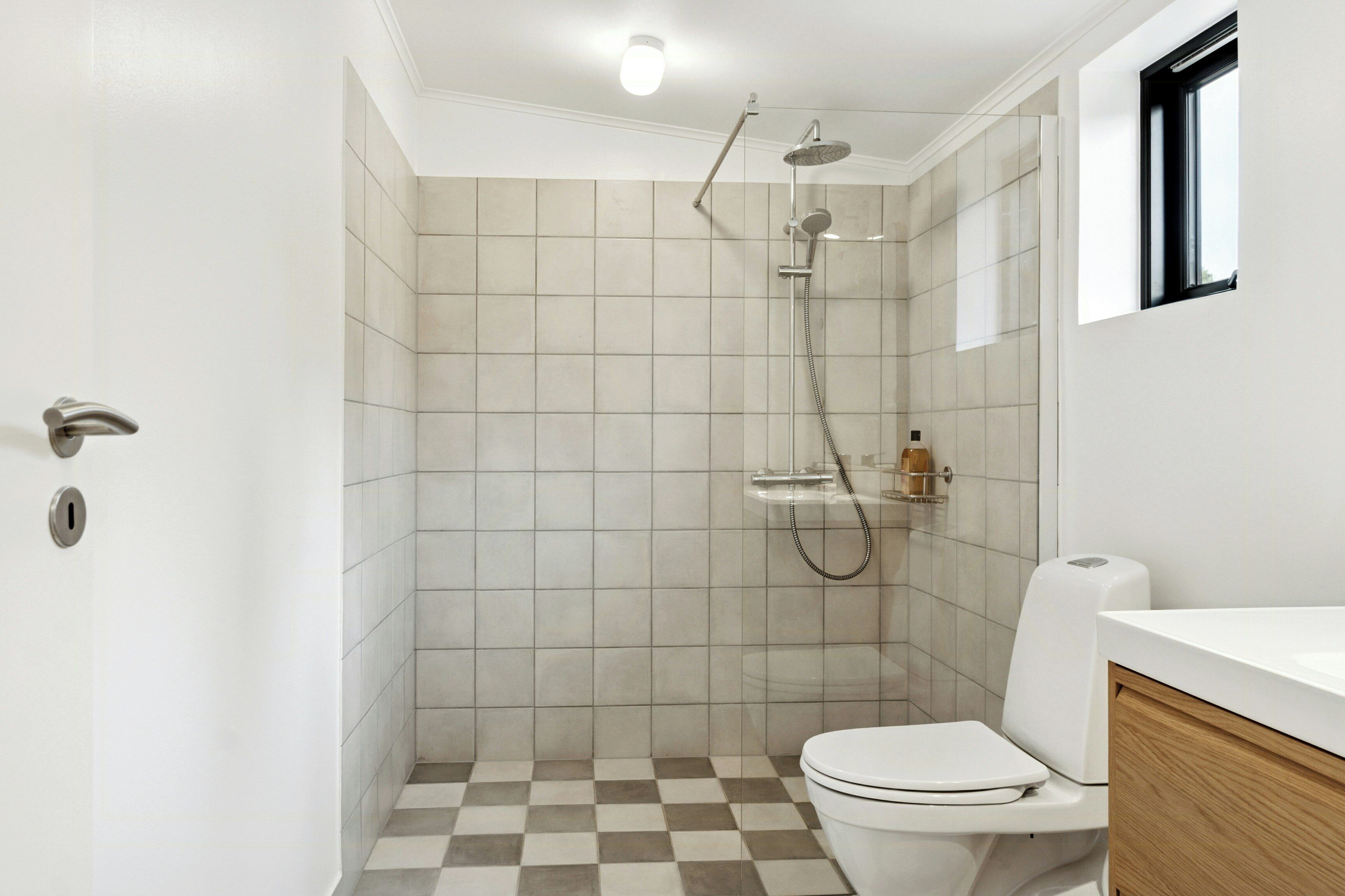 A bathroom with a checkered floor, a toilet, a shower with a handheld showerhead, and a white sink.