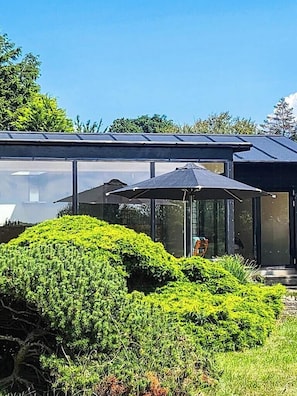 Eine moderne Glasarchitektur mit einer transparenten Dachkonstruktion, umgeben von gepflegter Bepflanzung.
